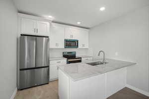 Kitchen with appliances with stainless steel finishes, light stone countertops, white cabinetry, a peninsula, and decorative backsplash