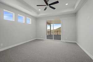 Carpeted empty room with a raised ceiling, a ceiling fan, and recessed lighting