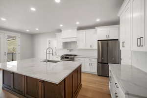 Kitchen with stainless steel appliances, light stone countertops, light wood-type flooring, white cabinets, and an island with sink