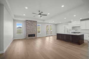 Kitchen featuring white cabinets, dark brown cabinetry, a kitchen island with sink, light wood-style floors, and open floor plan