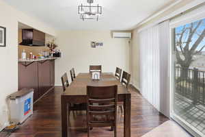 Dining area featuring dark wood-style flooring, a wall unit AC, and a chandelier