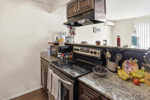 Kitchen featuring electric stove, light stone counters, dark brown cabinets, under cabinet range hood, and black microwave