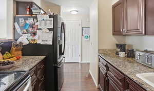 Kitchen featuring appliances with stainless steel finishes, light stone countertops, dark wood-style floors, and dark brown cabinets