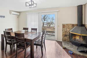 Dining area featuring hardwood / wood-style flooring, a wall unit AC, a wood stove, and a chandelier
