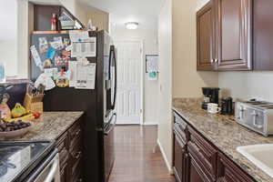 Kitchen with light stone countertops, stainless steel appliances, dark wood-type flooring, and a textured ceiling