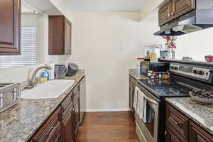 Kitchen featuring stainless steel appliances, dark brown cabinetry, and light stone countertops