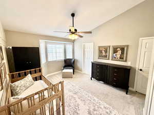 Bedroom featuring light carpet, vaulted ceiling, ceiling fan, and a crib