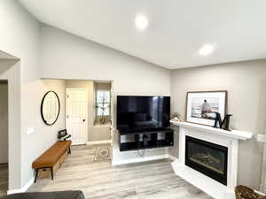 Living room with light wood-style flooring, lofted ceiling, and a glass covered fireplace