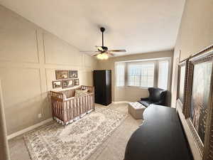 Carpeted bedroom with a crib, a decorative wall, a ceiling fan, and lofted ceiling