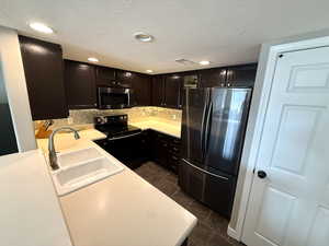 Kitchen with light countertops, appliances with stainless steel finishes, a textured ceiling, dark tile patterned floors, and dark cabinets