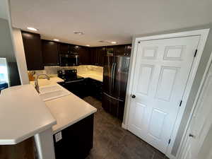 Kitchen featuring light countertops, appliances with stainless steel finishes, a peninsula, and dark cabinets