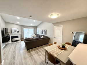 Dining area with light wood-type flooring, vaulted ceiling, a textured ceiling, and a fireplace