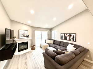 Living area featuring light wood finished floors, a glass covered fireplace, vaulted ceiling, and recessed lighting