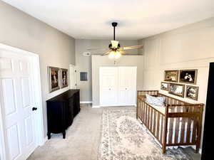 Bedroom with a crib, light carpet, a closet, ceiling fan, and electric panel