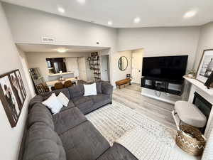 Living room with light wood-style flooring, high vaulted ceiling, recessed lighting, and a glass covered fireplace