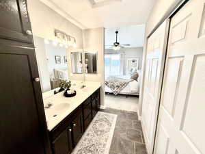 Full bath featuring double vanity, ensuite bathroom, a ceiling fan, and dark stone finish flooring