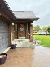 View of exterior entry featuring a yard, a shingled roof, brick siding, and covered porch