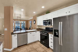 Kitchen with stainless steel appliances, white cabinetry, pendant lighting, a chandelier, and recessed lighting