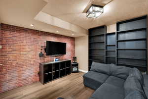 Living area featuring brick wall, light wood finished floors, a textured ceiling, recessed lighting, and an accent wall