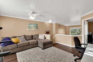 Living room with dark wood finished floors, an office area, ornamental molding, and ceiling fan