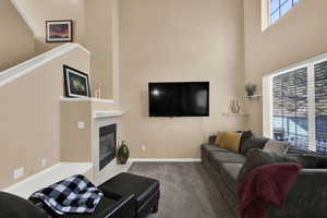 Living area with a tiled fireplace, carpet flooring, and a high ceiling