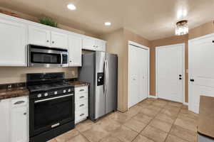 Kitchen featuring appliances with stainless steel finishes, dark countertops, white cabinets, and recessed lighting