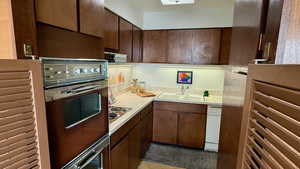 Kitchen with light countertops, dark brown cabinetry, double wall ovens, electric stovetop