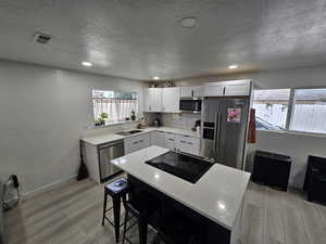 Kitchen with light wood-type flooring, stainless steel appliances, a breakfast bar area, a kitchen island, and a textured ceiling
