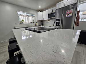 Kitchen featuring a center island, stainless steel appliances, light stone countertops, a kitchen breakfast bar, and white cabinetry