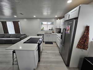 Kitchen featuring stainless steel appliances, open floor plan, a kitchen breakfast bar, white cabinetry, and recessed lighting