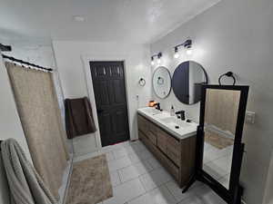 Full bath featuring a shower with shower curtain, double vanity, and a textured ceiling