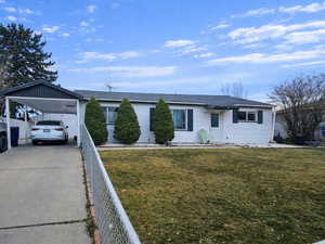 Single story home featuring driveway, an attached carport, a front yard, and a shingled roof