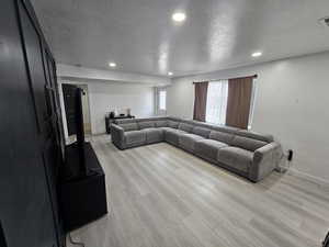 Living room with a textured ceiling, recessed lighting, and light wood-style flooring