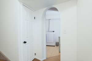 Basement hallway to laundry & basement bedroom. Featuring an arched walkway, light carpet, and light tile patterned flooring.