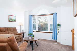 Carpeted living area with baseboards, chair rail trim, vaulted ceiling, and amazing picture window to watch the sunset.