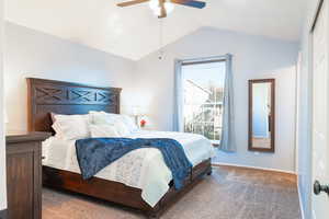 Primary bedroom with vaulted ceiling, ceiling fan, and carpet.