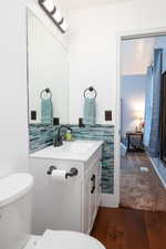 3/4 ensuite primary bathroom with vanity, dark wood-type flooring, and modern backsplash.
