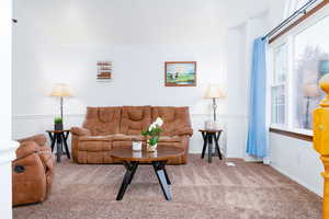 Carpeted living area with baseboards, chair rail trim, vaulted ceiling, and amazing picture window to watch the sunset.