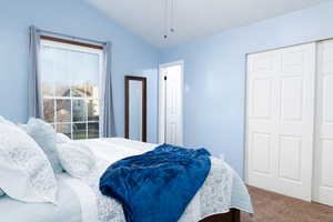 Primary bedroom with vaulted ceiling, ceiling fan, and carpet.