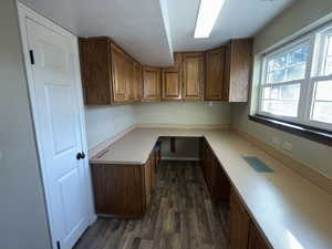 Basement office with built in desk and dark wood-style floors, oak cabinets, and above grade window.