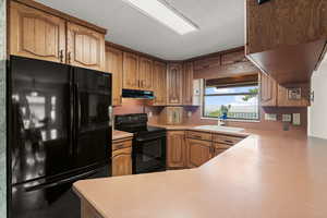 Kitchen with black appliances, light countertops, wood finish cabinetry, and a peninsula