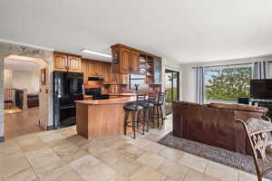 Kitchen with arched walkways, wood finish cabinets, black appliances, a kitchen breakfast bar, and glass insert cabinets