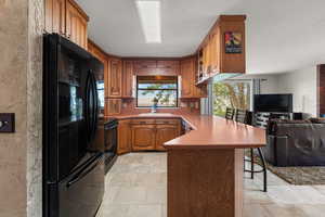 Kitchen with wood finish cabinetry, open floor plan, black appliances, light countertops, and a breakfast bar area