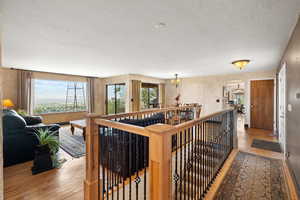Hall featuring an upstairs landing, arched walkways, light wood-style floors, a chandelier, and a textured ceiling