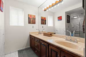 Bathroom with double vanity, a marble finish shower, and light marble finish flooring