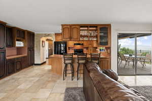 Kitchen with arched walkways, a kitchen bar, black appliances, a peninsula, and glass fronted cabinets