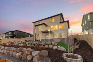 Back of house at dusk with a balcony, a fenced backyard, and stucco siding
