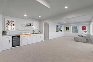 Indoor wet bar with open shelves, white cabinetry, beverage cooler, light carpet, and recessed lighting