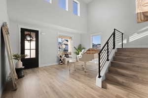 Entryway featuring stairs, light wood finished floors, healthy amount of natural light, and a towering ceiling