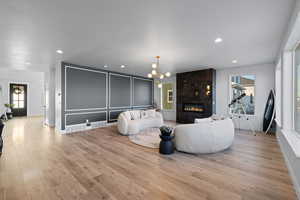 Living room with a premium fireplace, light wood finished floors, a chandelier, and recessed lighting